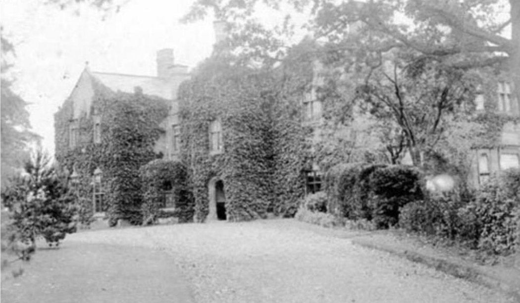 Early twentieth century photograph of Chorlton Hall, its entrance front entirely covered in ivy, the east extension now two storeys